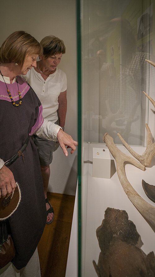 Museumsführung Die Museumsführerin erklärt einer Besucherin die Ausstellungsstücke in einem Schaukasten.