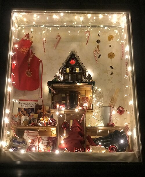 Adventsfenster Österberg Weihnachtlich dekoriertes Fenster mit Lichterkette, Lebkuchenhaus, Backutensilien und roten Weihnachtskugeln.