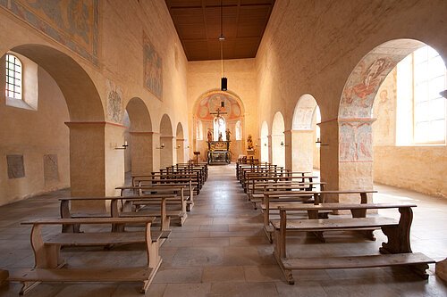 Basilika St. Martin in Greding Innenraum einer Kirche mit Holzbänken, Säulen und Altar im Hintergrund, helle Wände mit Fresken und Fenstern